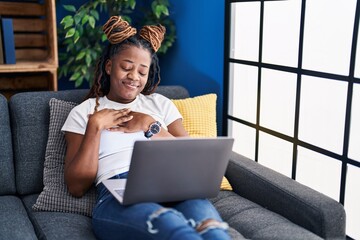 Poster - African woman with braided hair using laptop at home smiling with hands on chest, eyes closed with grateful gesture on face. health concept.