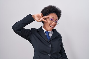 Wall Mural - Beautiful african woman with curly hair wearing business jacket and glasses doing peace symbol with fingers over face, smiling cheerful showing victory