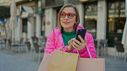 Sticker - Mature hispanic woman with grey hair smiling going shopping using smartphone at coffee shop terrace