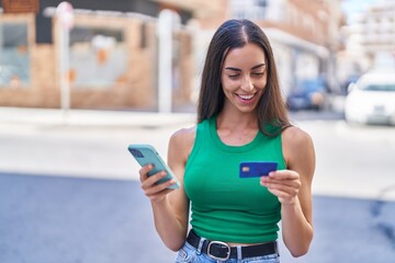 Wall Mural - Young beautiful hispanic woman using smartphone and credit card at street