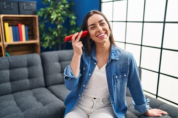 Poster - Young beautiful hispanic woman listening voice message by smartphone sitting on sofa at home