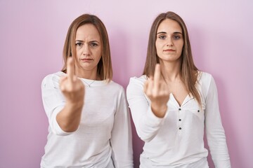 Wall Mural - Middle age mother and young daughter standing over pink background showing middle finger, impolite and rude fuck off expression