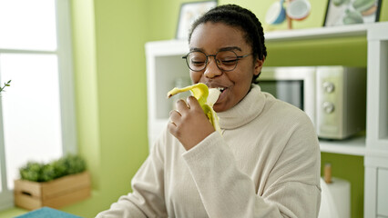 Wall Mural - African american woman smiling confident eating banana at dinning room