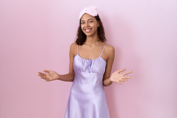 Poster - Young hispanic woman wearing sleep mask and nightgown smiling cheerful with open arms as friendly welcome, positive and confident greetings