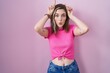 © Krakenimages.com - Blonde caucasian woman standing over pink background doing funny gesture with finger over head as bull horns