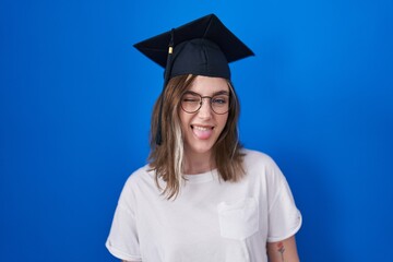 Wall Mural - Blonde caucasian woman wearing graduation cap sticking tongue out happy with funny expression. emotion concept.