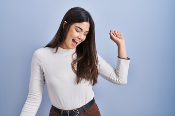 Canvas Print - Young brunette woman standing over blue background dancing happy and cheerful, smiling moving casual and confident listening to music