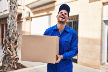 Sticker - Young hispanic man delivering box smiling and laughing hard out loud because funny crazy joke.