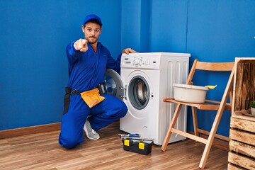 Poster - Young hispanic man working on washing machine pointing with finger to the camera and to you, confident gesture looking serious