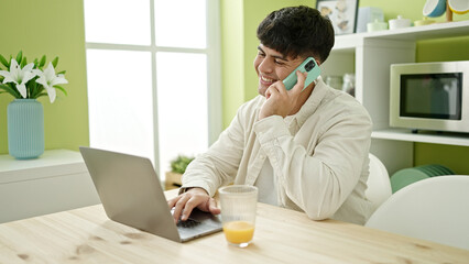 Sticker - Young hispanic man using laptop talking on smartphone sitting on table at dinning room