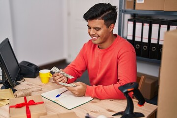 Poster - Young hispanic man ecommerce business worker using laptop counting dollars at office