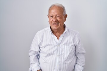 Wall Mural - Senior man with grey hair standing over isolated background winking looking at the camera with sexy expression, cheerful and happy face.