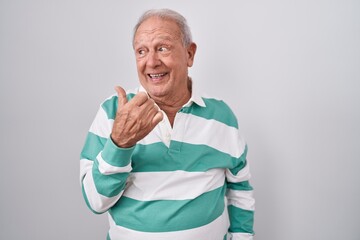 Sticker - Senior man with grey hair standing over white background smiling with happy face looking and pointing to the side with thumb up.