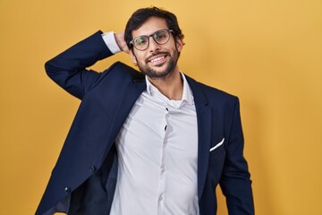 Wall Mural - Handsome latin man standing over yellow background smiling confident touching hair with hand up gesture, posing attractive and fashionable