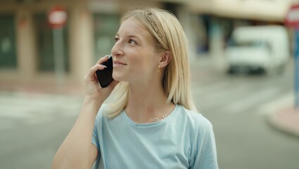 Wall Mural - Young blonde woman smiling confident talking on the smartphone at street