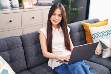 Canvas Print - Young chinese woman using laptop sitting on sofa at home