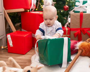 Sticker - Adorable caucasian baby unpacking gift sitting on floor by christmas tree at home