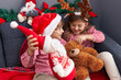 © Krakenimages.com - Brother and sister playing with teddy bear and santa claus doll sitting on sofa by christmas decoration at home