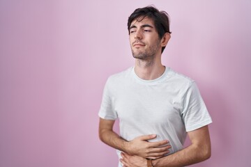 Canvas Print - Young hispanic man standing over pink background with hand on stomach because indigestion, painful illness feeling unwell. ache concept.