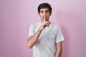 Poster - Young hispanic man standing over pink background asking to be quiet with finger on lips. silence and secret concept.