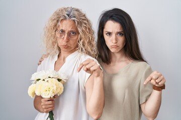 Poster - Mother and daughter holding bouquet of white flowers pointing down looking sad and upset, indicating direction with fingers, unhappy and depressed.