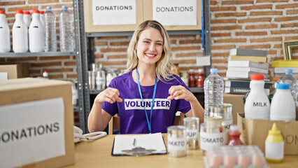 Poster - Young blonde woman sitting on table pointing herself to volunteer uniform at charity center