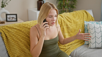 Poster - Young blonde woman speaking on the phone sitting on sofa arguing at home