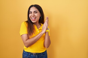 Wall Mural - Young arab woman standing over yellow background clapping and applauding happy and joyful, smiling proud hands together