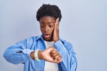 Sticker - African american woman standing over blue background looking at the watch time worried, afraid of getting late