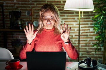 Canvas Print - Blonde woman using laptop at night at home showing and pointing up with fingers number nine while smiling confident and happy.