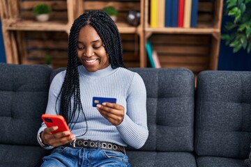 Poster - African american woman using smartphone and credit card sitting on sofa at home