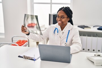 Poster - African american woman doctor looking xray sitting on table at clinic