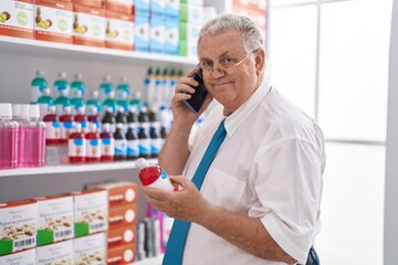 Poster - Middle age grey-haired man customer talking on smartphone holding medication bottle at pharmacy