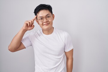 Sticker - Young asian man standing over white background smiling pointing to head with one finger, great idea or thought, good memory