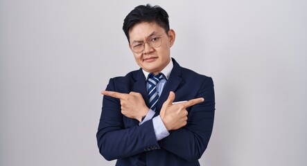 Sticker - Young asian man wearing business suit and tie pointing to both sides with fingers, different direction disagree