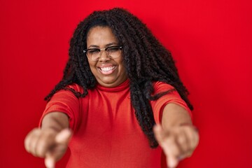 Canvas Print - Plus size hispanic woman standing over red background pointing to you and the camera with fingers, smiling positive and cheerful