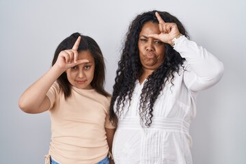 Canvas Print - Mother and young daughter standing over white background making fun of people with fingers on forehead doing loser gesture mocking and insulting.