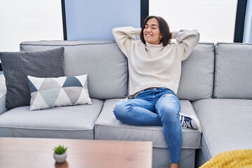 Poster - Young hispanic woman relaxed with hands on head sitting on sofa at home