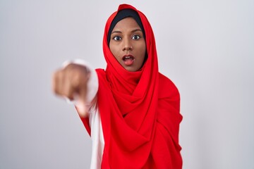 Wall Mural - Young arab woman wearing traditional islamic hijab scarf pointing with finger surprised ahead, open mouth amazed expression, something on the front