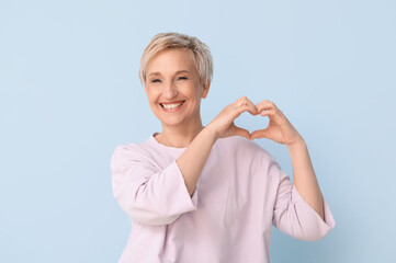 Poster - Mature blonde woman making heart with hands on blue background