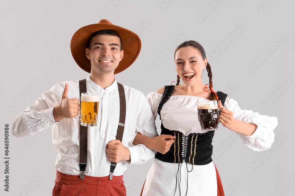 Young couple in traditional German clothes with beer on light background
