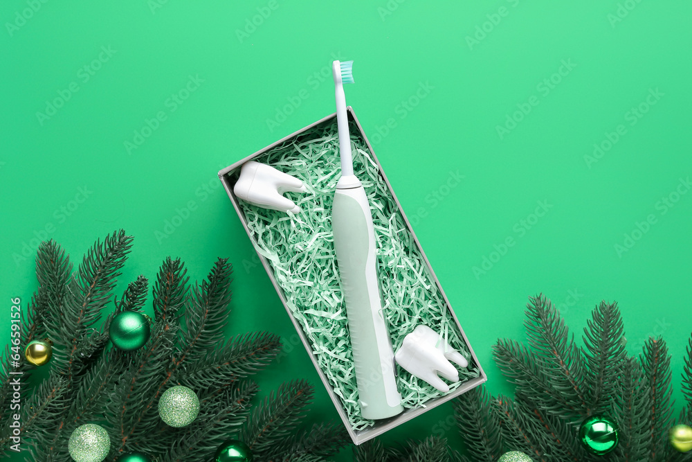 Gift box with electric toothbrush, plastic teeth and Christmas branches on green background
