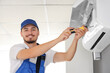 © Pixel-Shot - Male technician fixing air conditioner in room