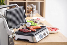 Electric Grill With Tasty Sausages On Table In Kitchen