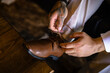 groom with hand tattoos tying brown leather dress shoe