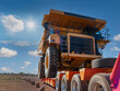 industrial trailer carrying a huge mining truck on a dirt road in the outback , sunny day