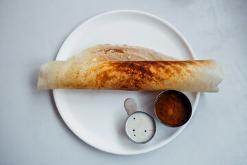 Crispy crepes made of little millets and lentils. Commonly known as little millet dosa. Plated as dosa rolls. Served with coconut spicy condiments and sambar. White background