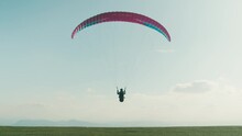 Professional Paraglider Run And Take Off From Edge Of Mountain Into Blue Sky. Slow Motion Shot Of Man Use Paragliding Parachute To Fly