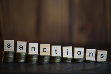 Poster - Word Sanctions made of wooden block letters with coins stacks