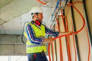 Wall Mural - An experienced electrician who stands on a ladder and adjusts cable bellows for the electrical network of the building where he works.